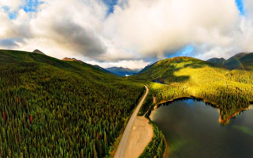 Panoramic View of Scenic Road alongside Peaceful Lake surrounded by Mountains in Canadian Nature. Aerial Drone Shot. Taken near Stewart-Cassiar Highway, Northern British Columbia, Canada.