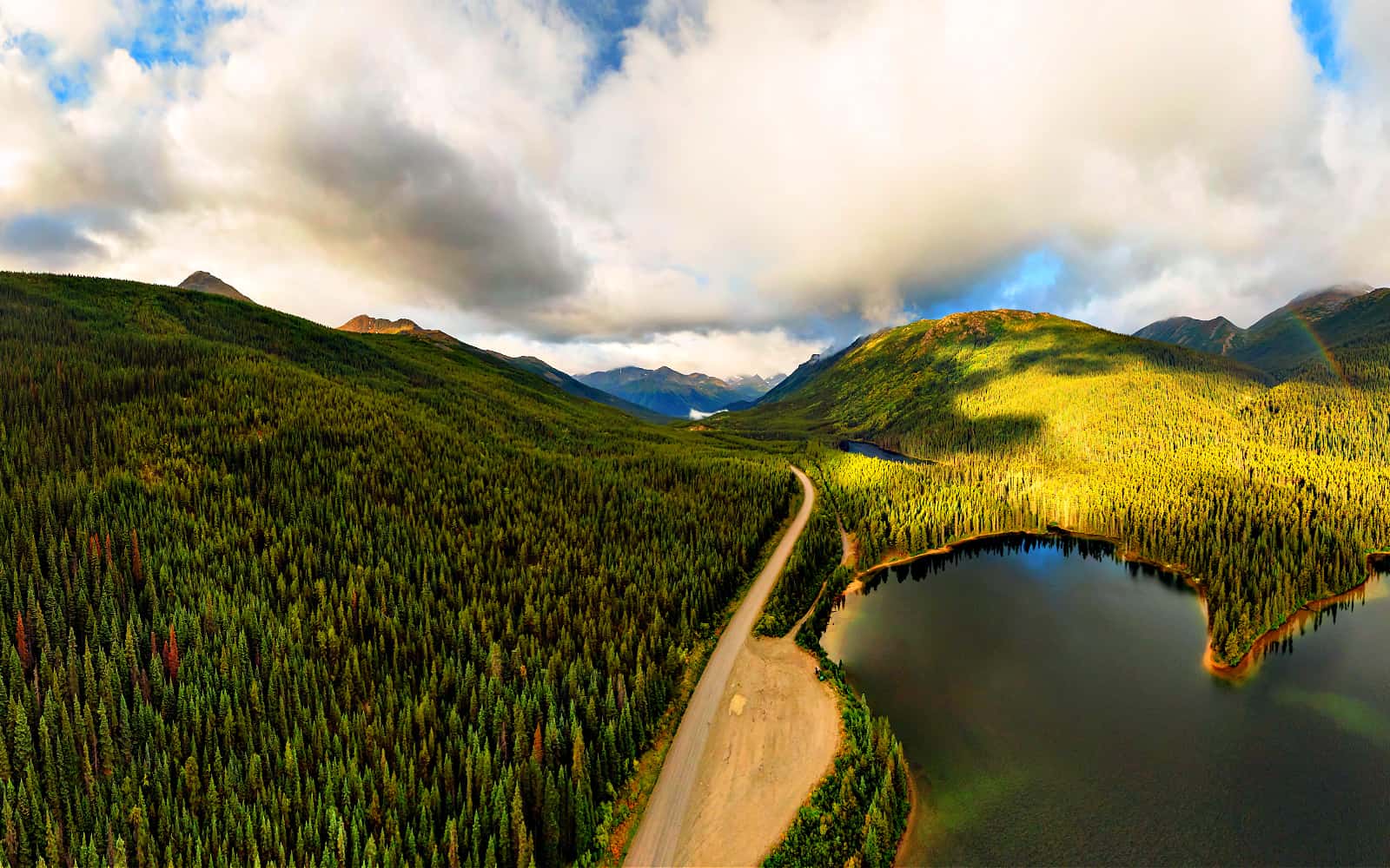 Panoramic View of Scenic Road alongside Peaceful Lake surrounded by Mountains in Canadian Nature. Aerial Drone Shot. Taken near Stewart-Cassiar Highway, Northern British Columbia, Canada.