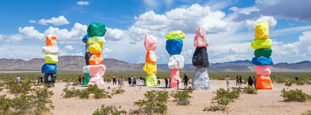 Seven Magic Mountains art installation near Las Vegas city. Pillars made of neon colored boulders stand against barren desert background and blue sky.