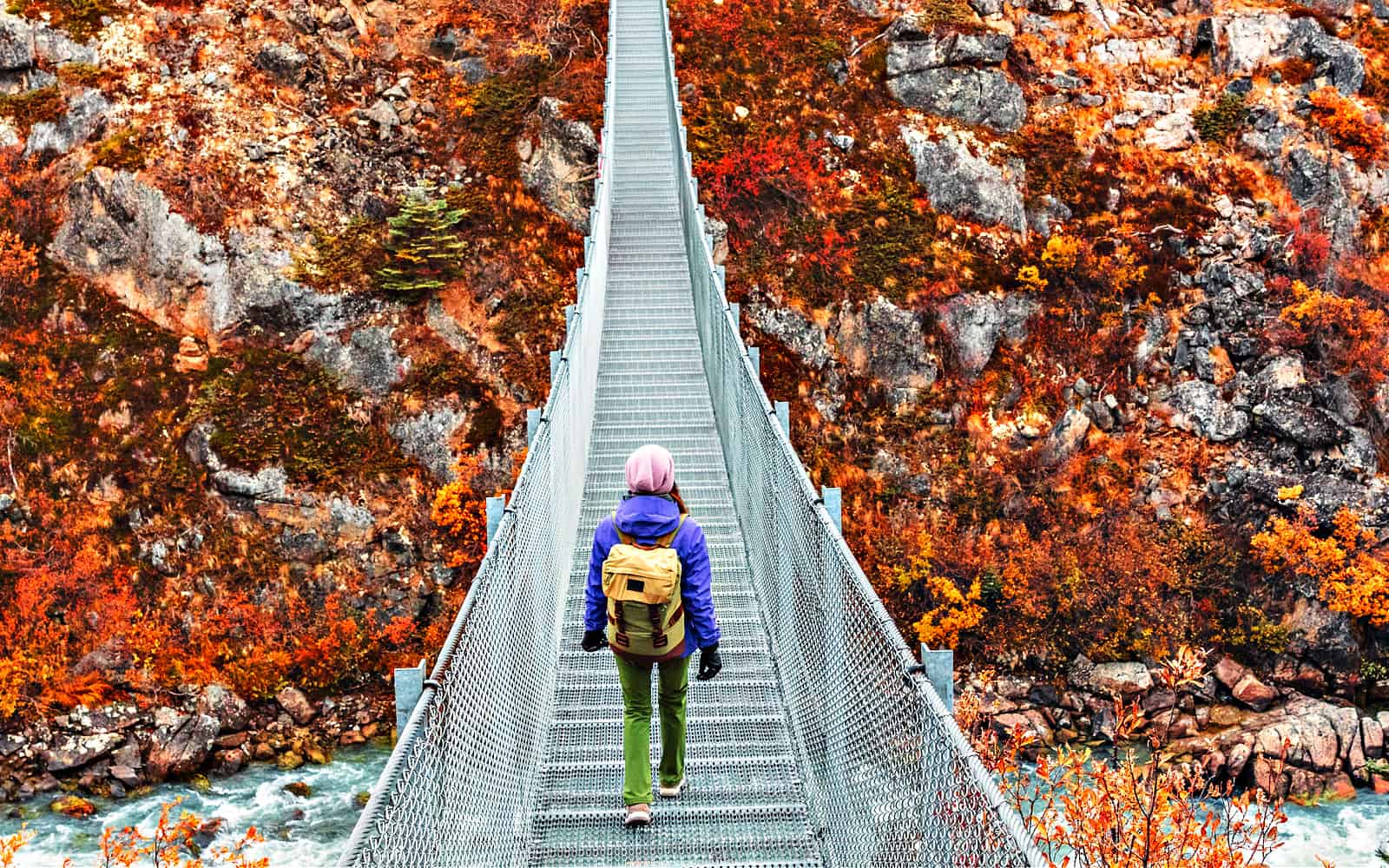 Canada travel hiker walking across Yukon River Suspension bridge. Explore the Canadian North.Cruise tour from Skagway, Alaska.