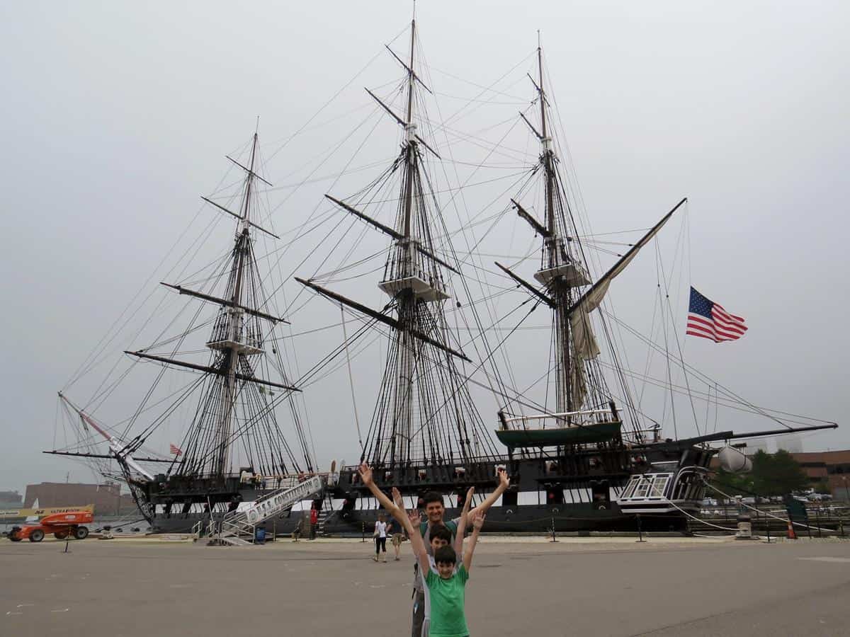 Father happily raising their arms while taking a picture with the USS Constitution