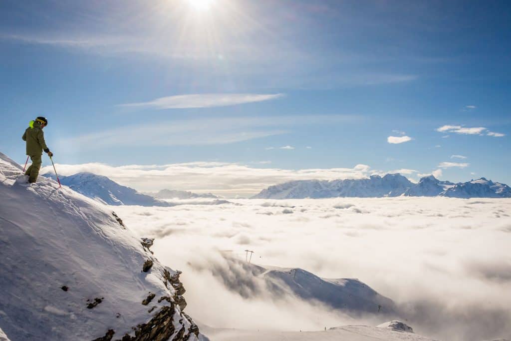 A Skier standing on the side of a mountain seeing the breathtaking scenery of the clouds beneath him