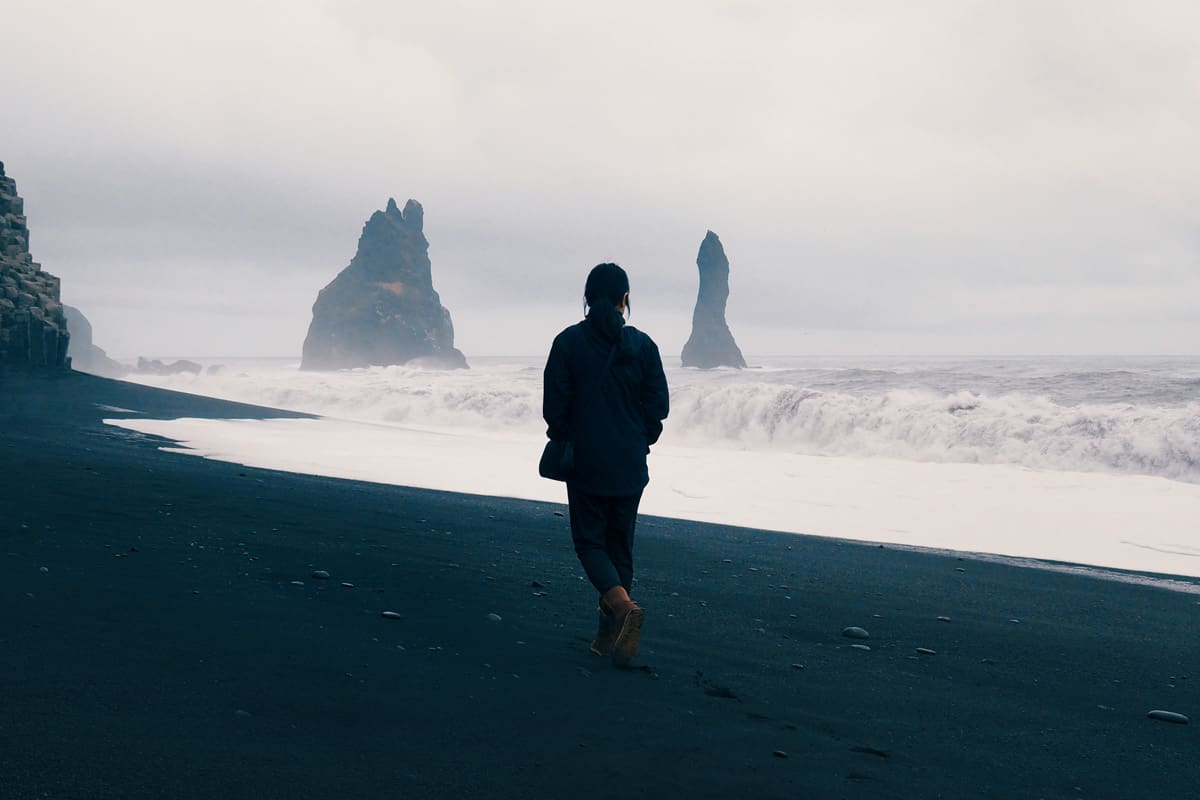 Woman walking alone on black sand beach at Reynisfjara, Iceland., How Much Money Do You Need Per Day In Iceland? [Tips For Your Travel]