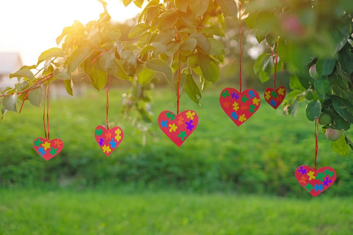 Cards in the shape of hearts with multicolored bright puzzle pieces inside hang on apple tre