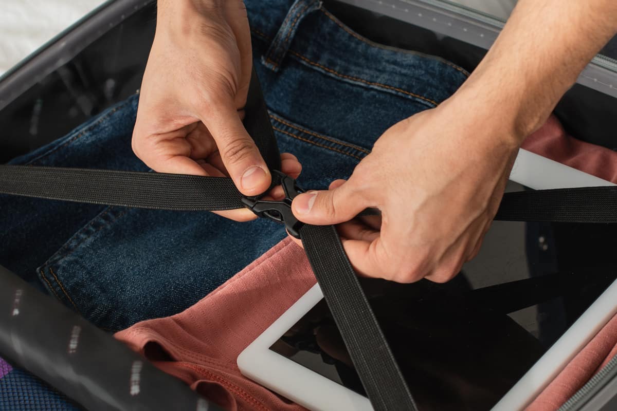 Cropped view of man locking belts of suitcase on bed, banner, 10 Must Have Gadgets For Your Next Trip!