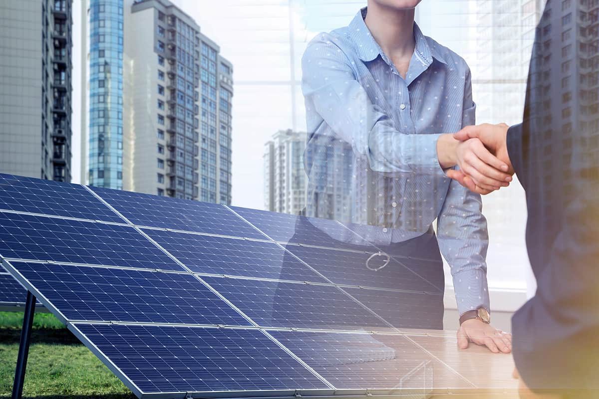 Double exposure of businesspeople shaking hands and solar panels installed outdoors