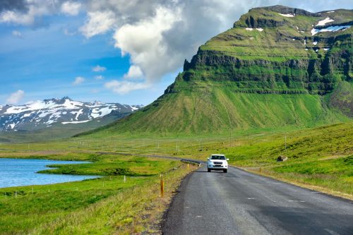 White cars running on a curved road The background is a great mountain with green grass all over the area. During the summer in Iceland, Road trip concepts and driving in traveling. - Baths In Iceland - Driving Trip Planner [Inc. Sample Itineraries]