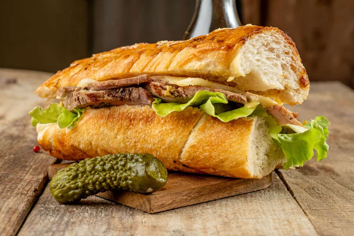 A mouth-watering big Cuban sandwich with baked pork, cheese and pickled cucumbers in a toasted baguette.