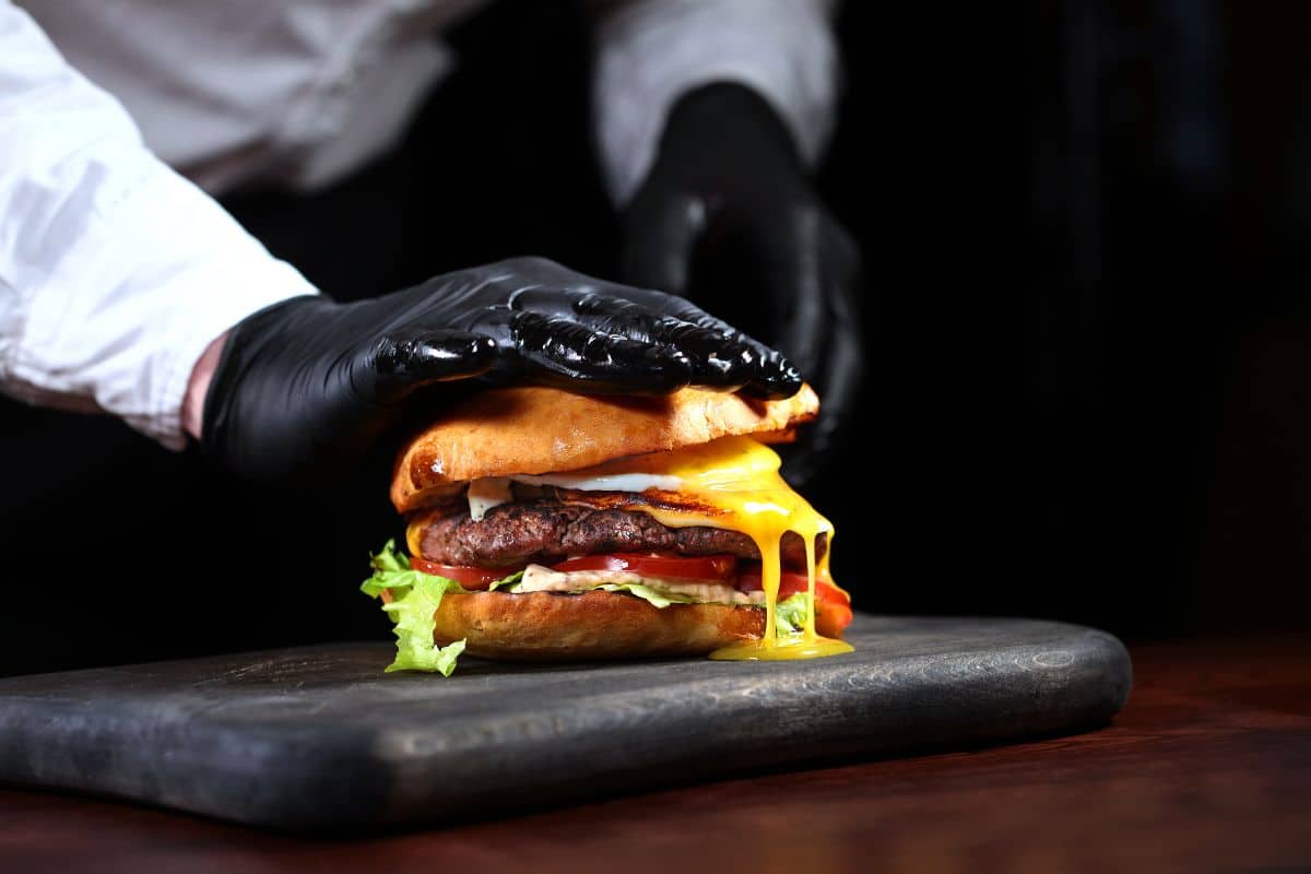 Chef in black gloves cooking a hamburger. Horizontal photo. An unrecognizable photo on a black background. - Discover the Mouth-Watering Pesto Provolone Burger in North Miami