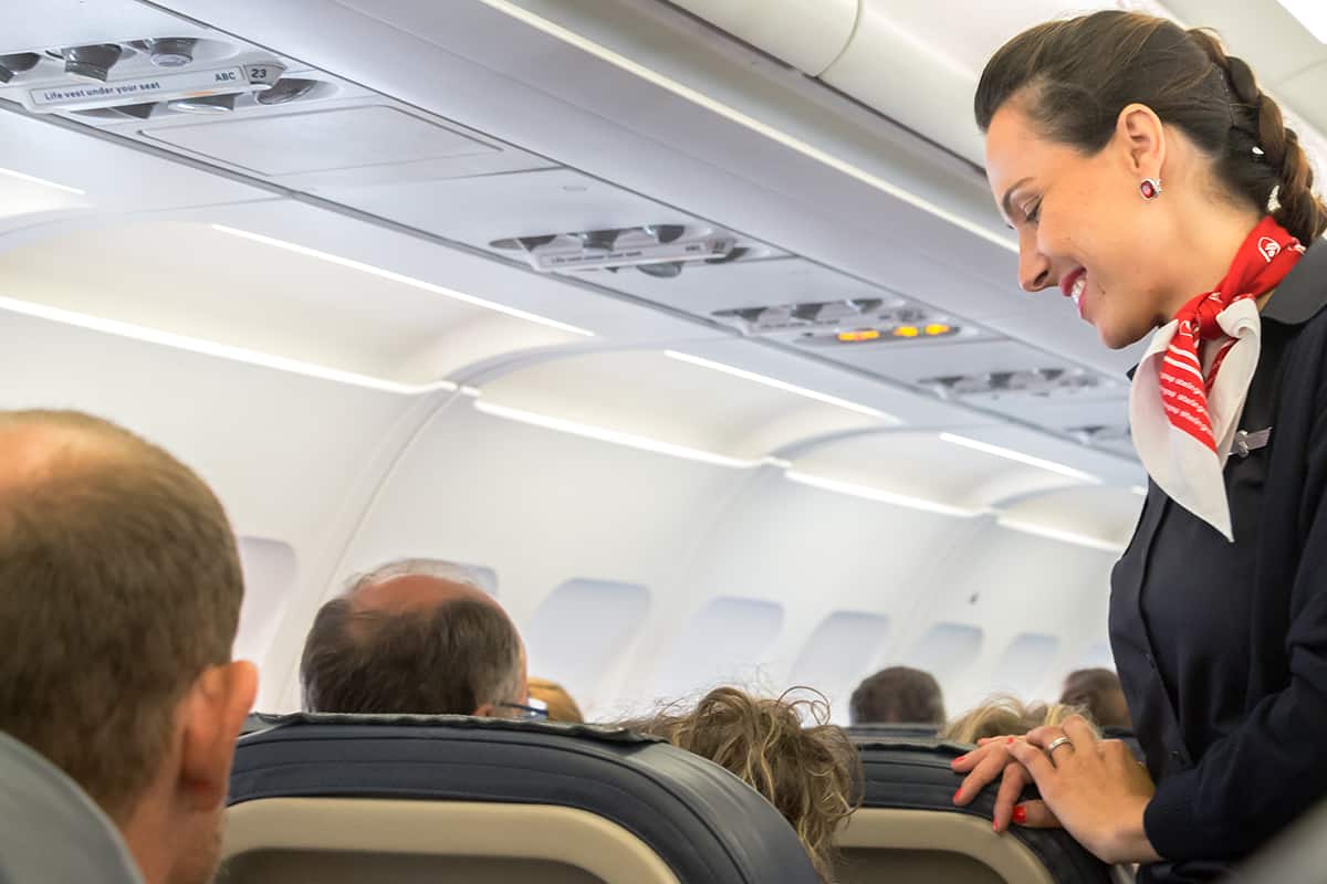 Female flight attendant is speaking with a passenger sitting in the economy class