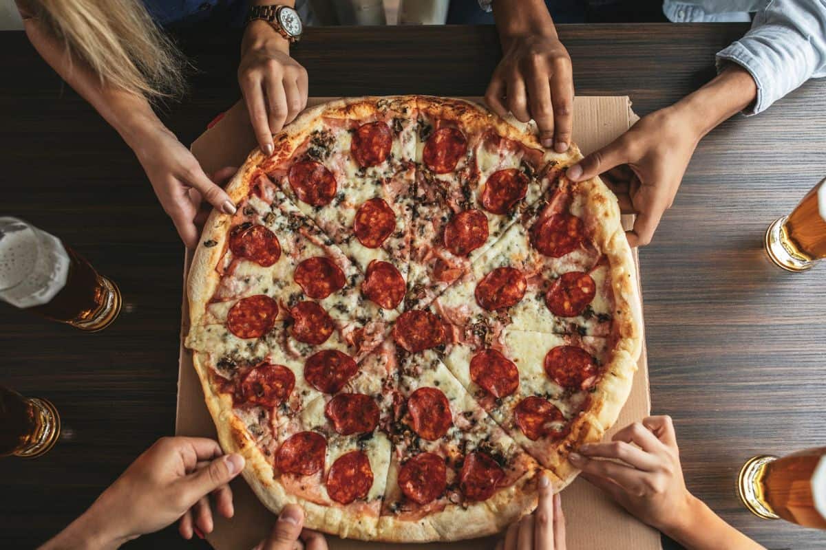 High angle shot of a group of unrecognizable people's hands each grabbing a slice of pizza