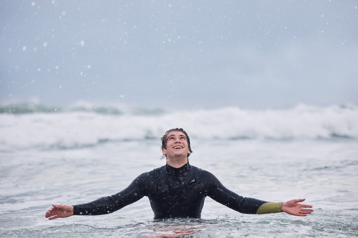 Surfing, sports and man in ocean during rain enjoy nature, spring weather and swimming in waves.