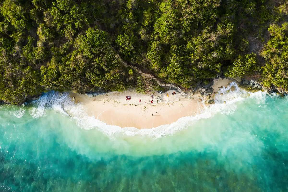 View from above, stunning aerial view of some tourists sunbathing on a beautiful beach bathed by a turquoise rough sea during sunset, Green Bowl Beach, South Bali, Indonesia.