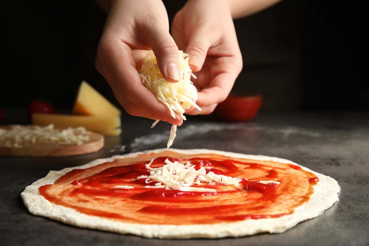 Woman adding cheese to pizza at grey table, closeup