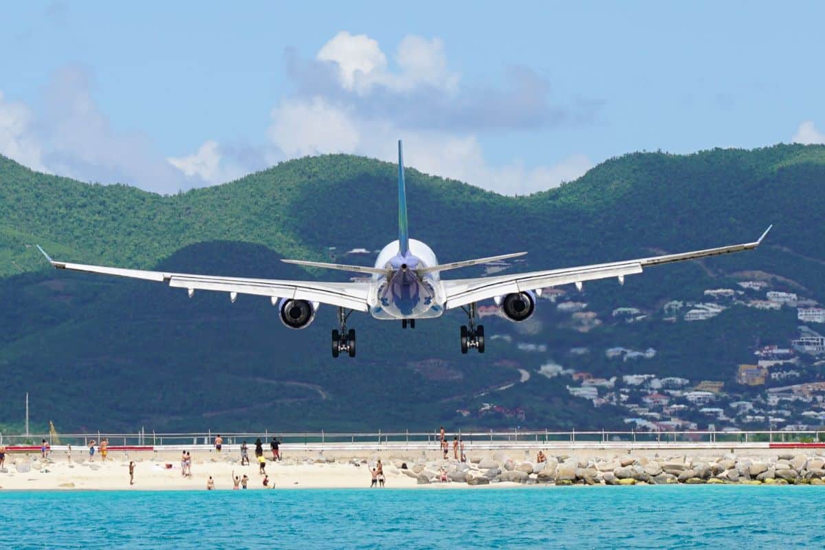 Airplane flying over people during landing at Maho Beach in Saint Maarten at Princess Juliana airport. Unique view of commercial plane landing.
