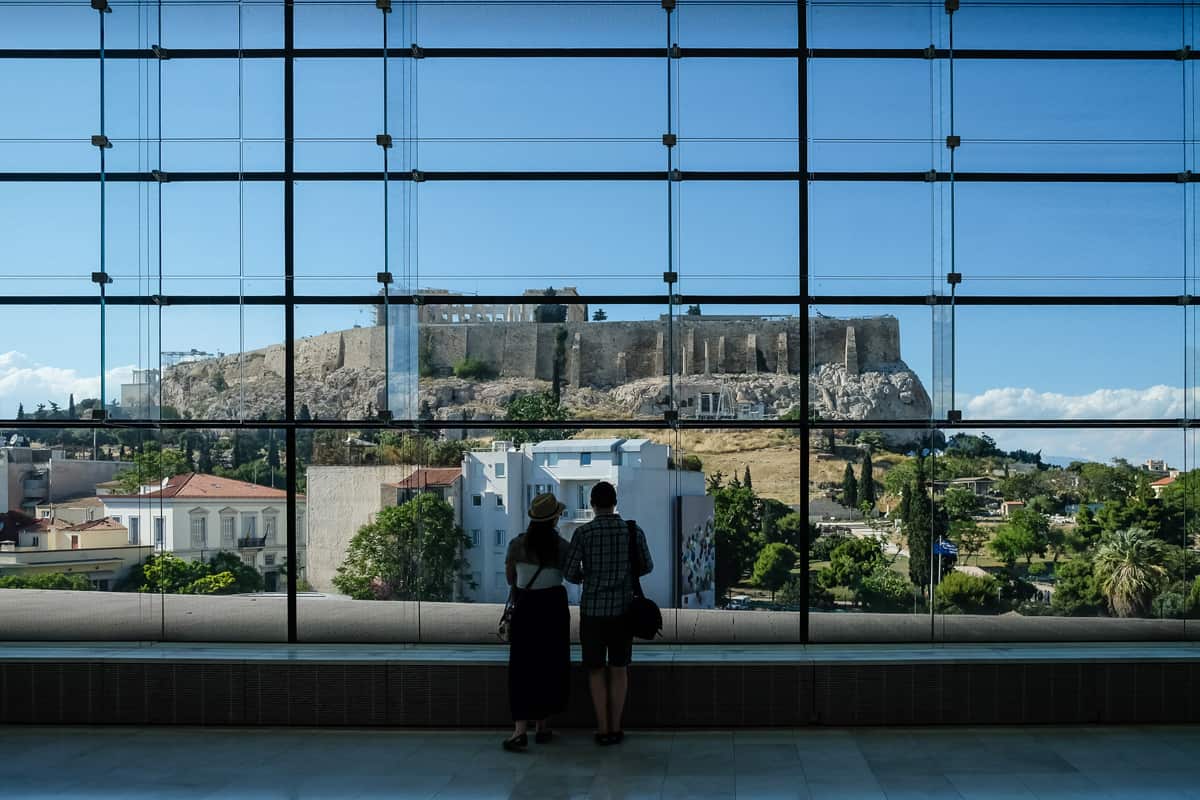 Couple looking out at the Acropolis throught huge glass window in the Acropolis Museum. Athens, Greece.