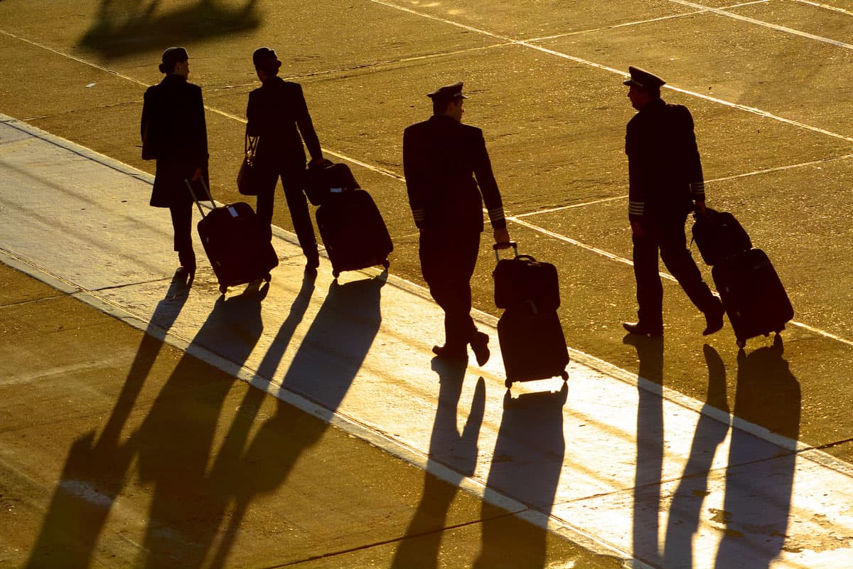 Flight attendants and pilots walking with bags. Professionals of aviation including cabin crew and pilot silhouette early in the morning with long shades., Revealed: The Best Kept Travel Secret of Flight Crews