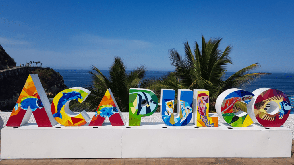 Acapulco, Mexico - April 9, 2019: Beautiful colorful Acapulco inscription sign with bright colorful letters and blue ocean and trees as background.