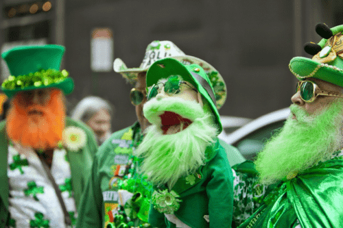 Image is of a group of individuals outside for a St. Patrick's Day parade. They are dressed head to toe for the festivities. One appears to be a puppet.