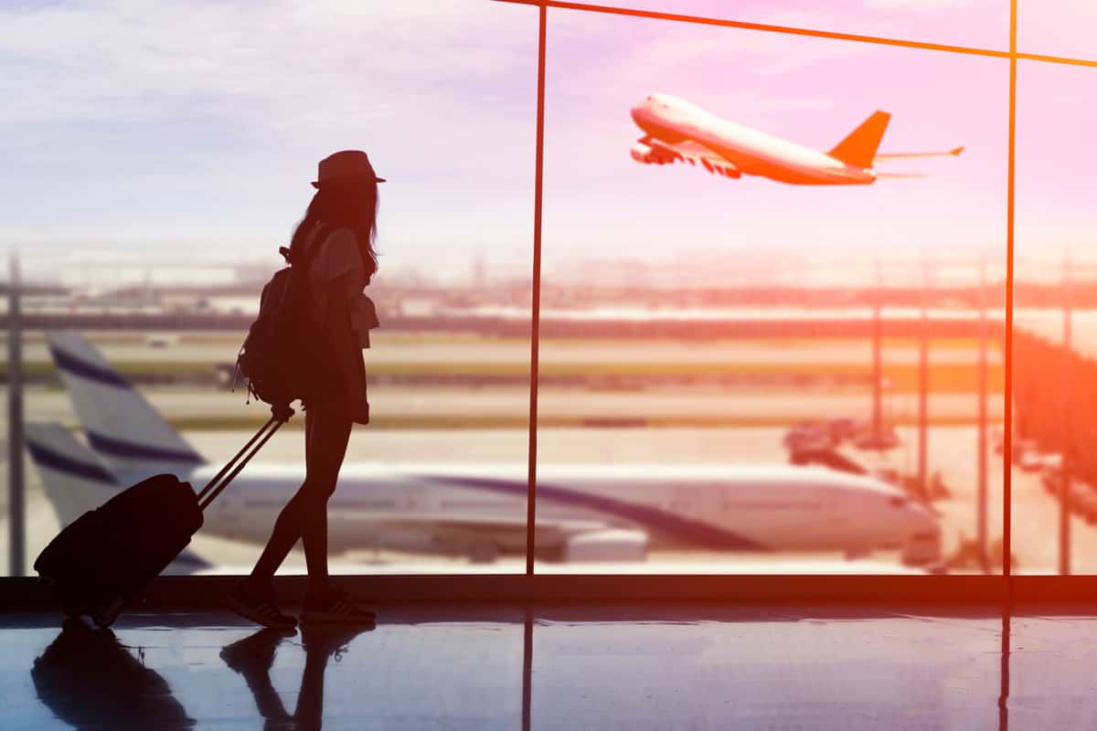 Young woman is standing near window at the airport and watching plane before departure