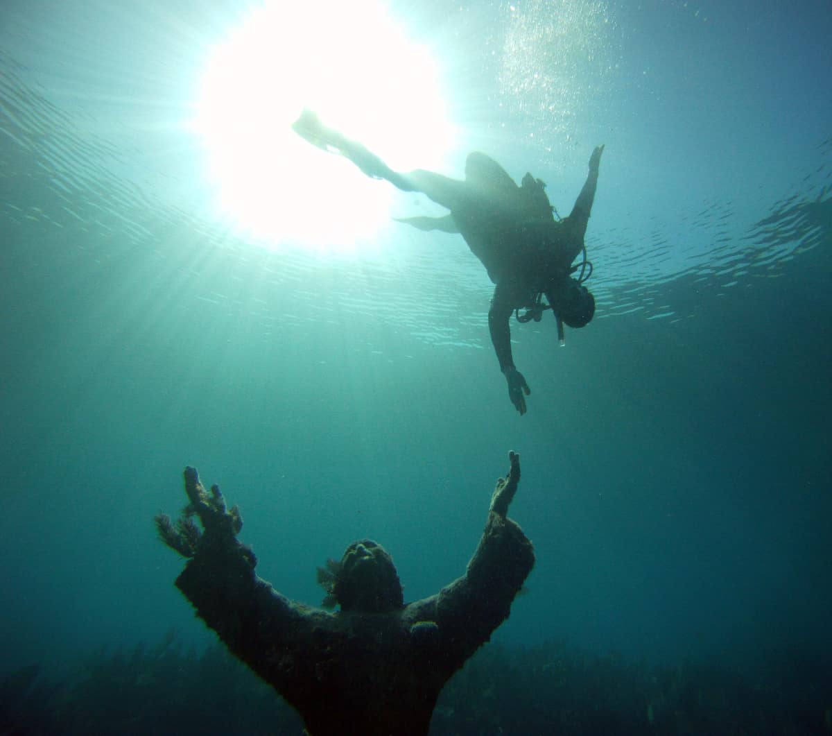 Scuba diver reaching down to Christ of the Abyss in Florida