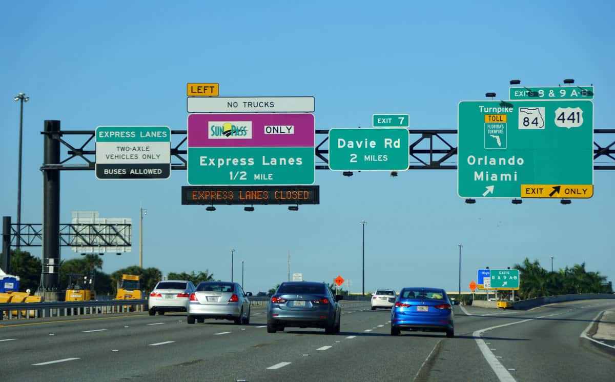 The view of four-lane traffic on 95 North with signs into Sunpass toll and Florida Turnpike into Orlando from Miami