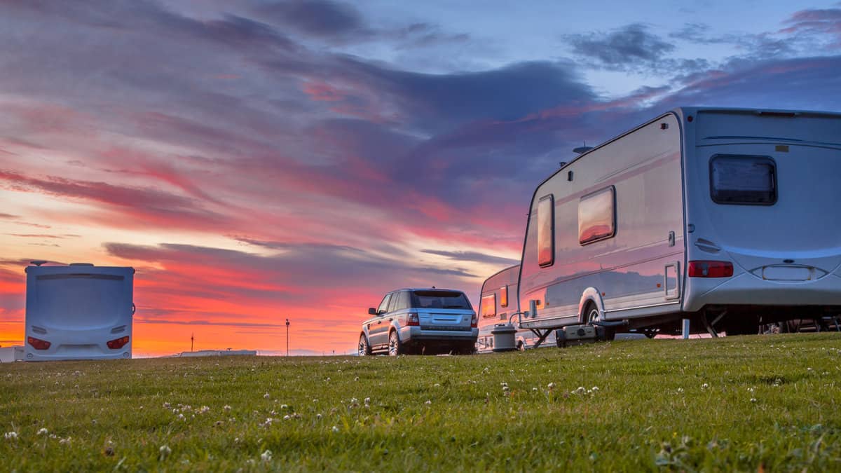 Camping caravans and cars parked on a grassy campground under beautiful sunset 1600x900