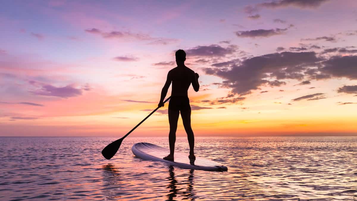Person stand up paddle boarding at dusk on a flat warm quiet sea with beautiful sunset colors