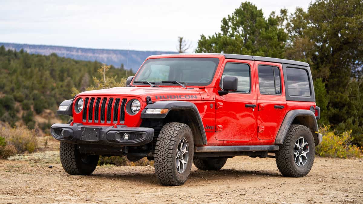 Red Jeep Wrangler Rubicon parked on a dirt road in the Colorado wilderness with overcast sky