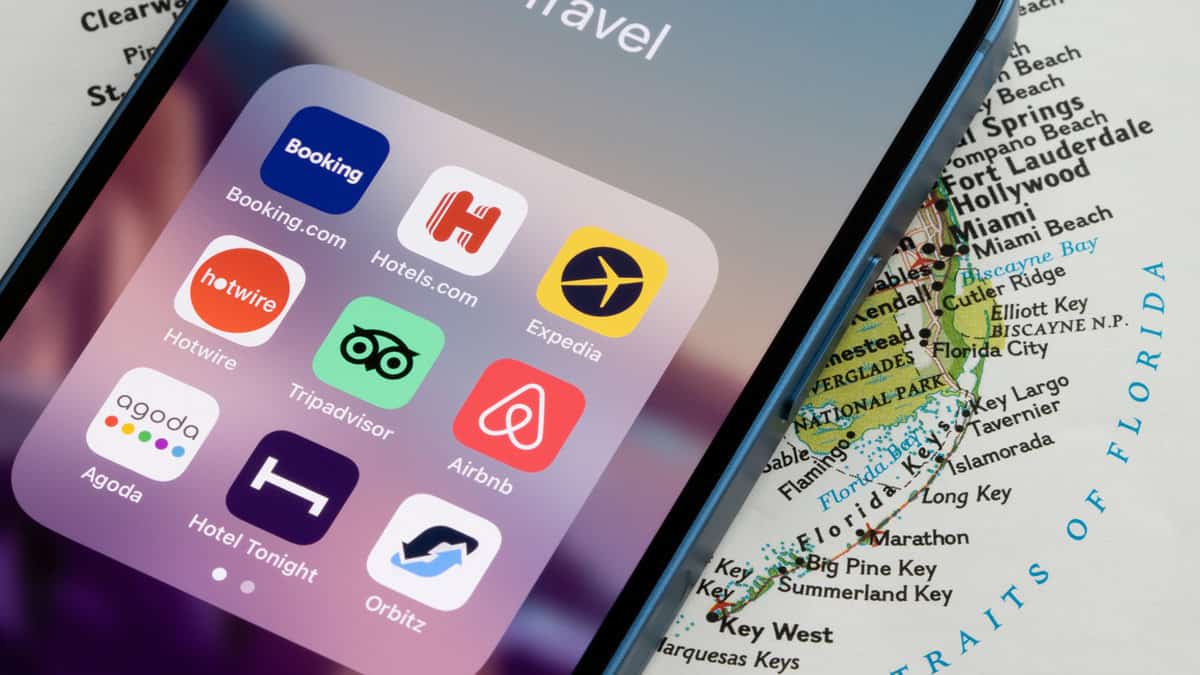 Assorted travel apps are seen on an iPhone, including Booking.com, Hotels.com, Expedia, Hotwire, Tripadvisor, Airbnb, Agoda, Hotel Tonight, and Orbitz.
