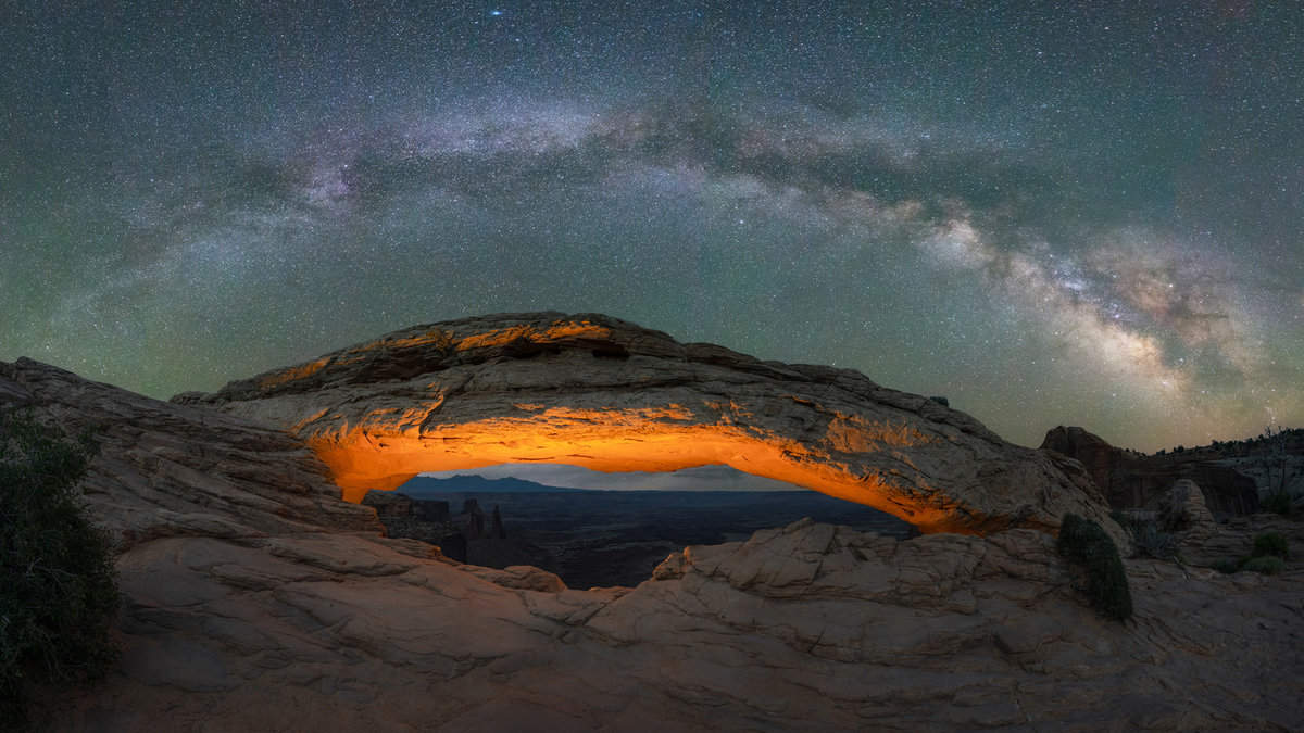 Milky Way Galaxy panorama over a lit Mesa Arch in Canyonlands National Park