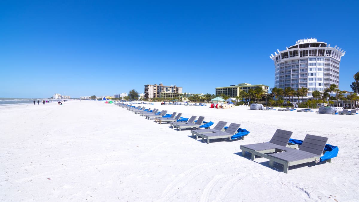 Resort and hotel lounge chairs lined up on clean, white sand under clear, blue sky at beautiful St. Pete Beach in St. Petersburg, Florida
