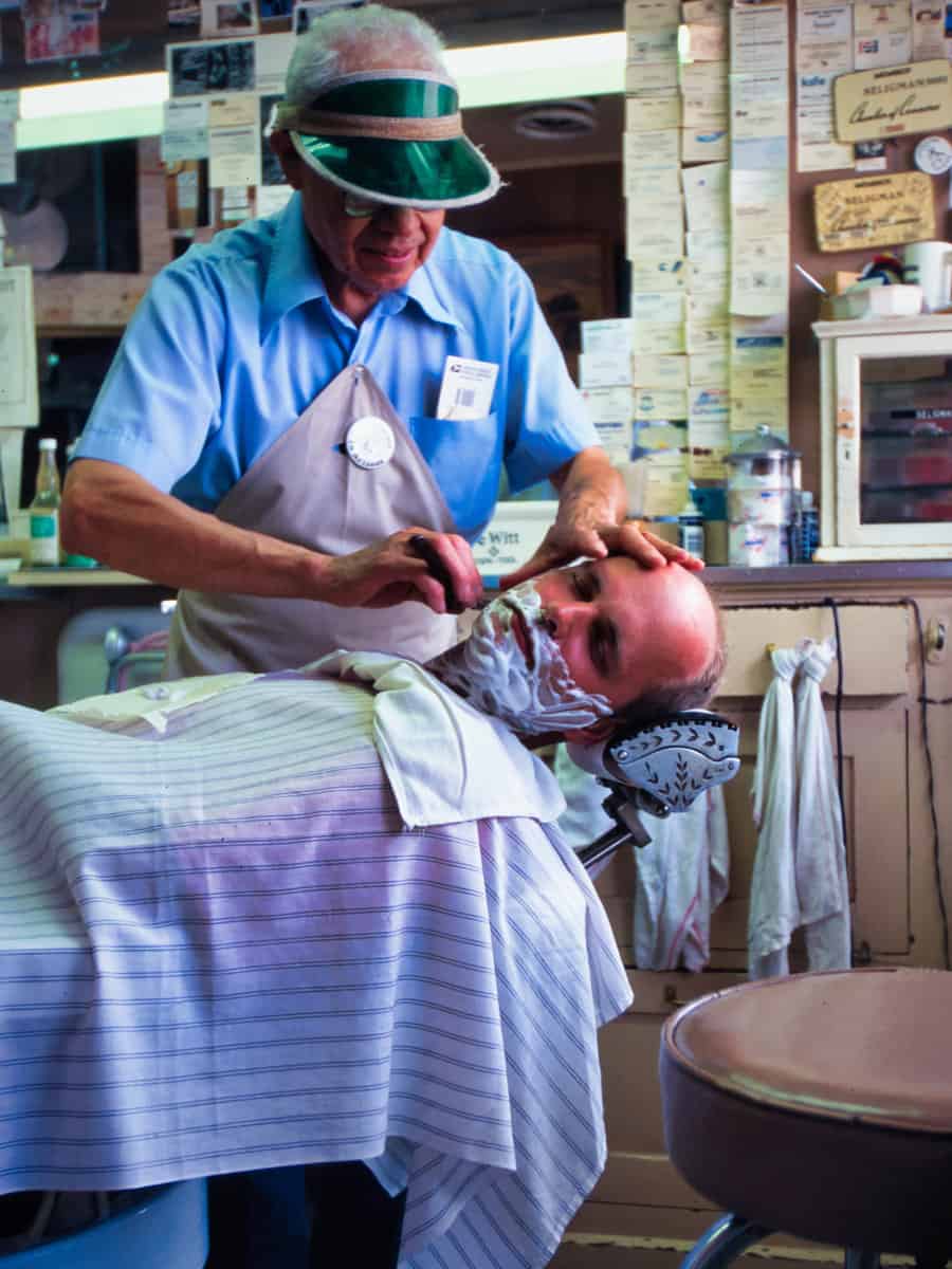 1995 picture of barber Angel Delgadillo, shaving a client in his shop in Seligman.