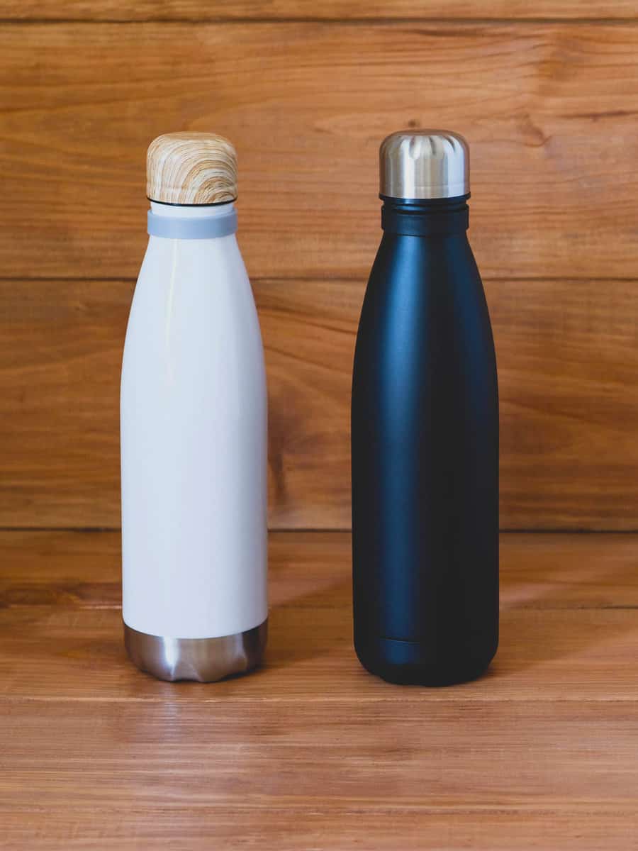 Reusable eco-friendly black and white stainless steel thermo bottles on wooden rustic background