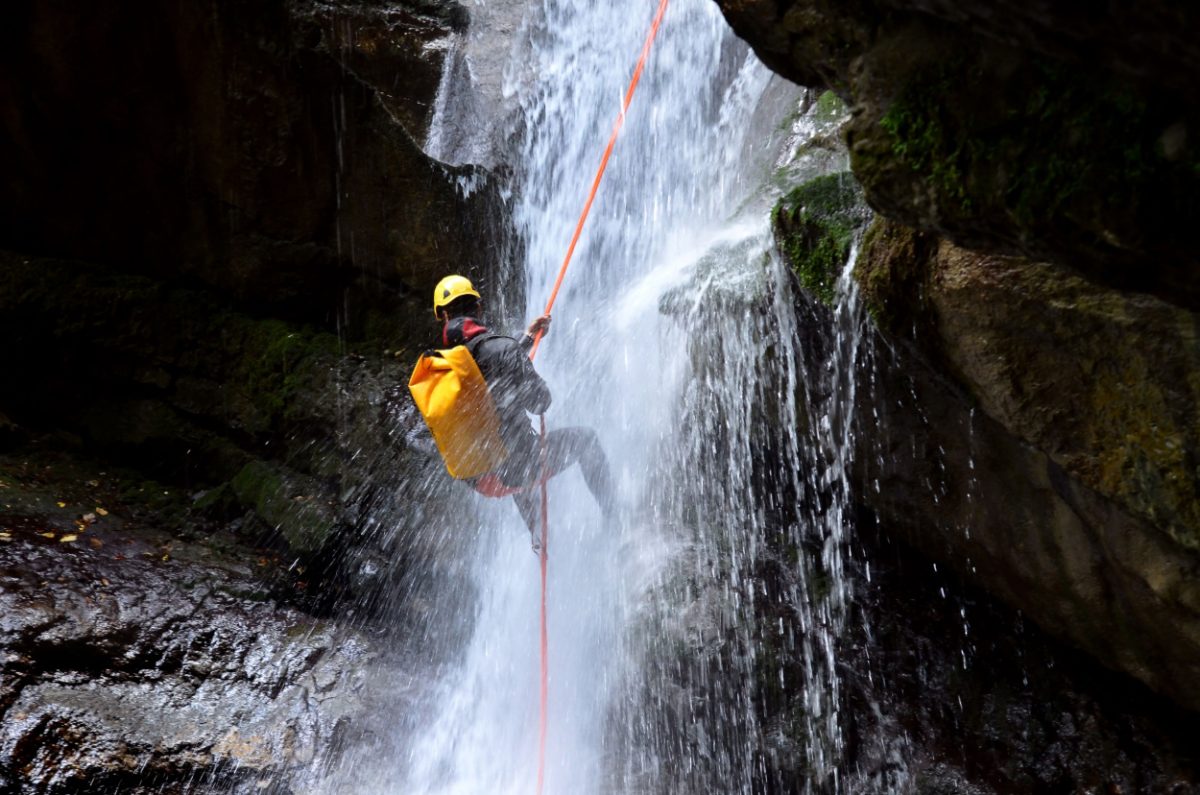 Man hanging of a rope at the bottom of a waterfall