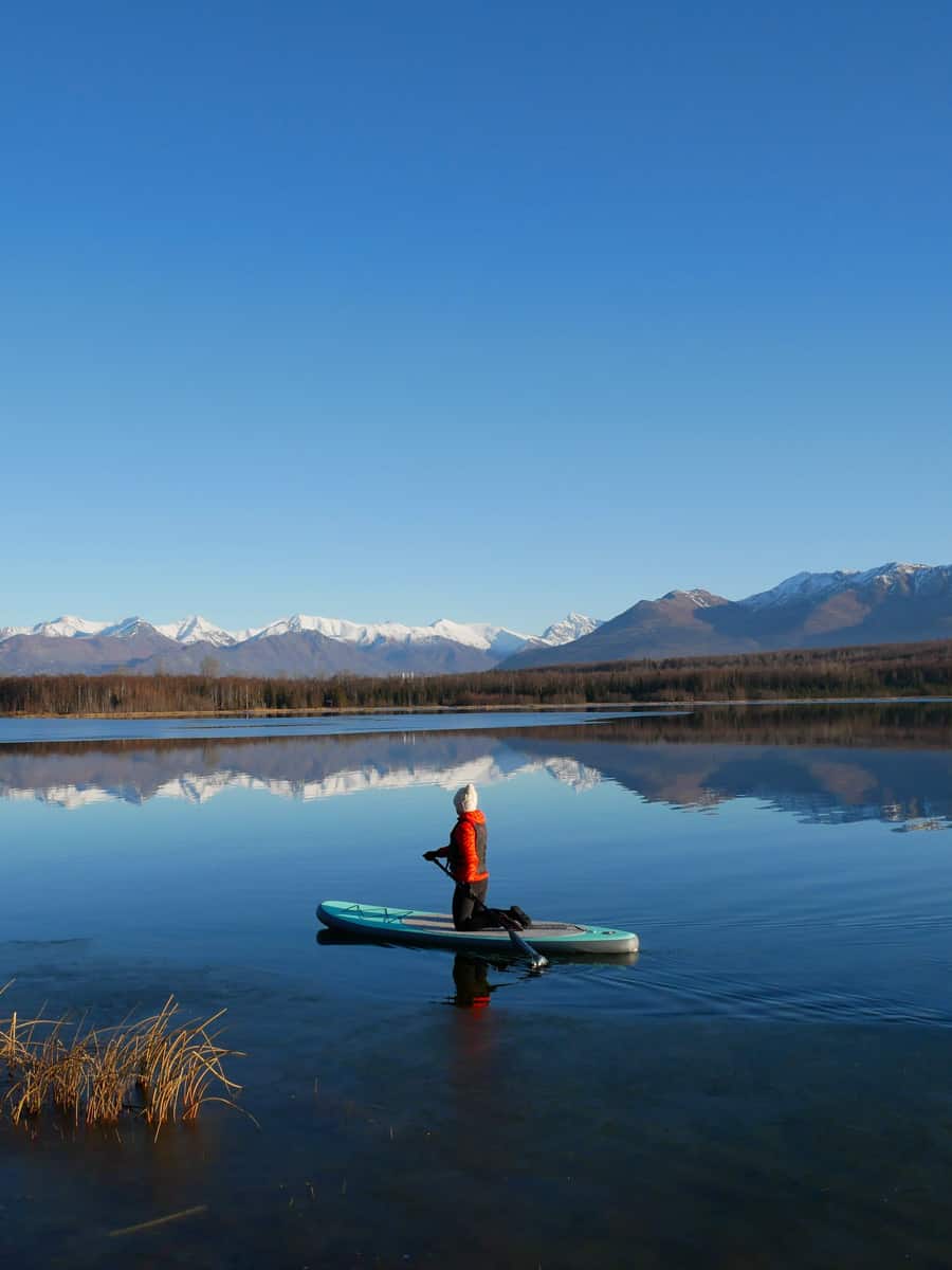 A woman paddle boarding on an Alaska lake in the fall