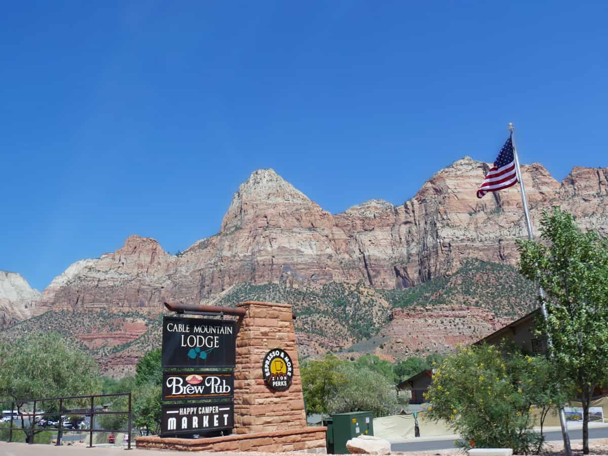  Road side sign of the Cable Mountain Lodge and Drew Pub at Springdale, with steep red cliffs of Zion National Park in the background.