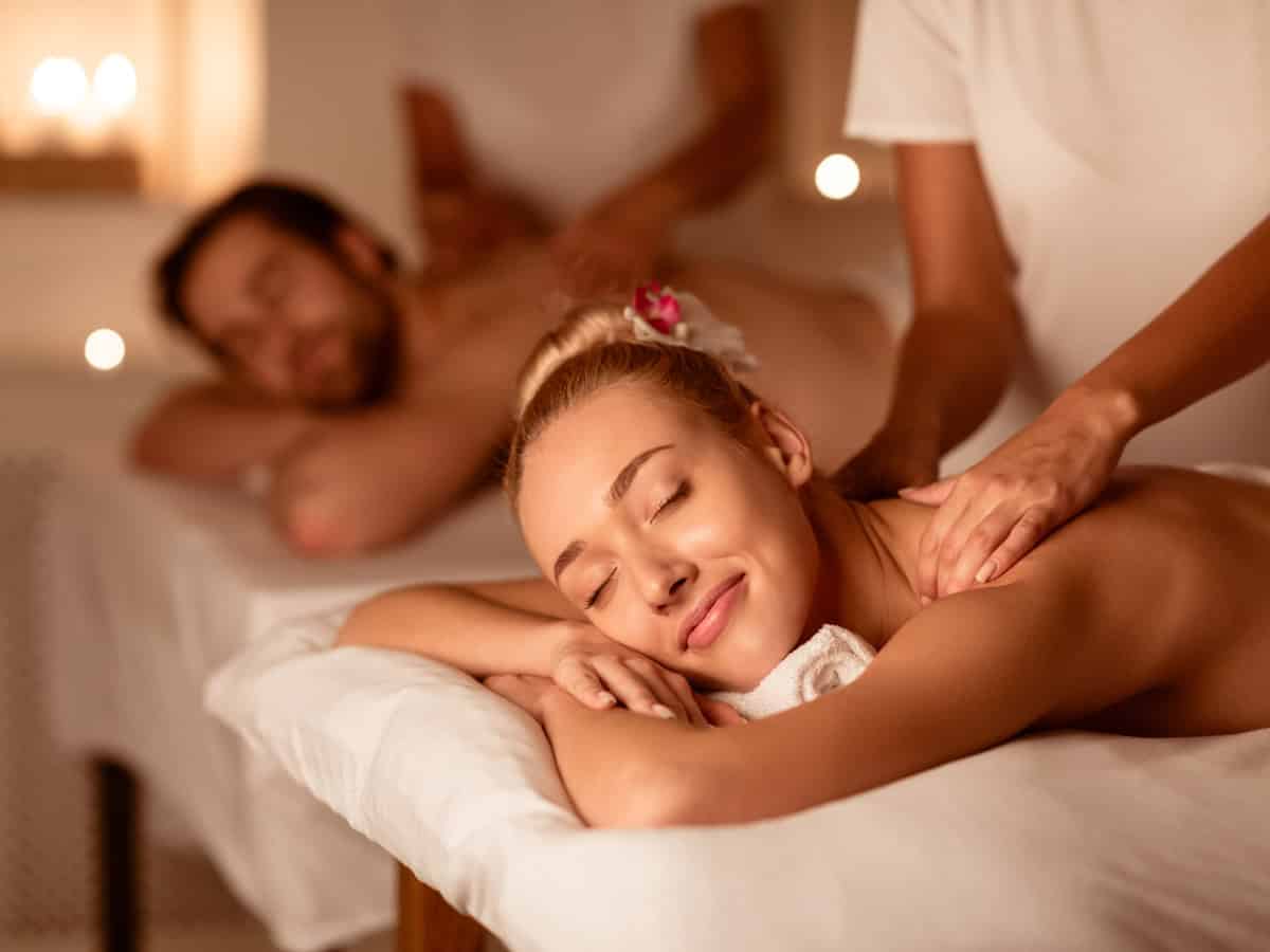 Couple Relaxing Receiving Back Massage Lying Closing Eyes At Romantic Luxury Spa With Burning Candles And Flowers