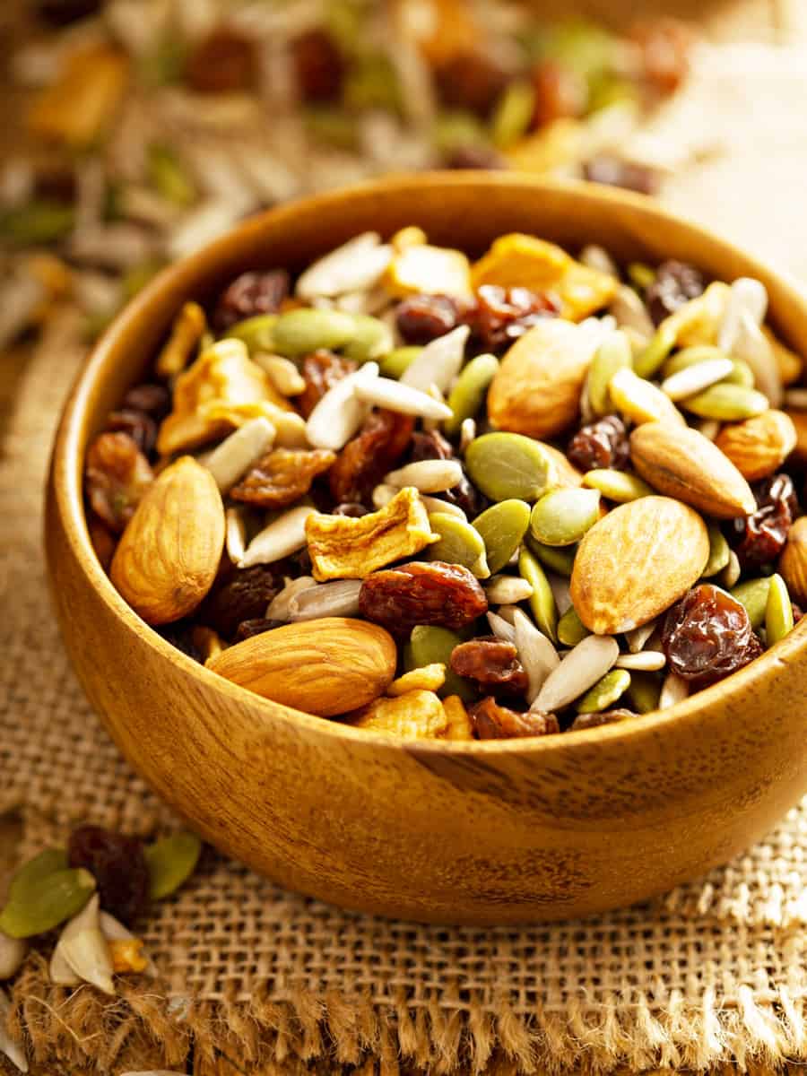 Dried fruit and nuts trail mix with almonds, raisins, seeds and apples in a wooden bowl
