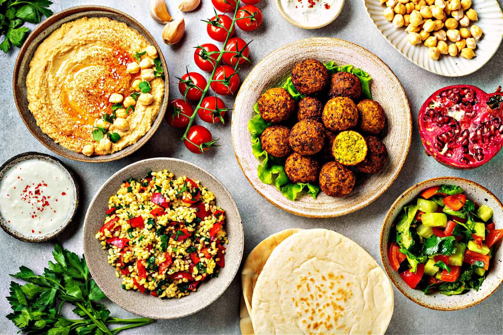 falafel, hummus, tabouleh, pita and vegetables on a concrete background, view from above